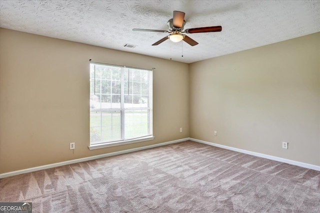 carpeted empty room with a textured ceiling, baseboards, visible vents, and ceiling fan