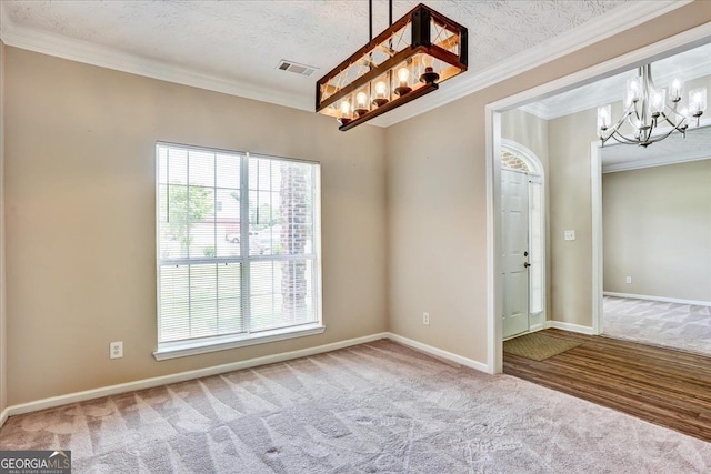 carpeted spare room with crown molding, a notable chandelier, baseboards, and visible vents