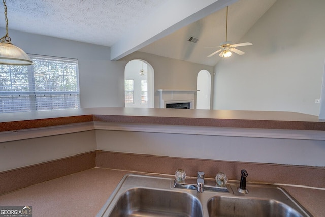 kitchen featuring visible vents, ceiling fan, vaulted ceiling, a fireplace, and a sink