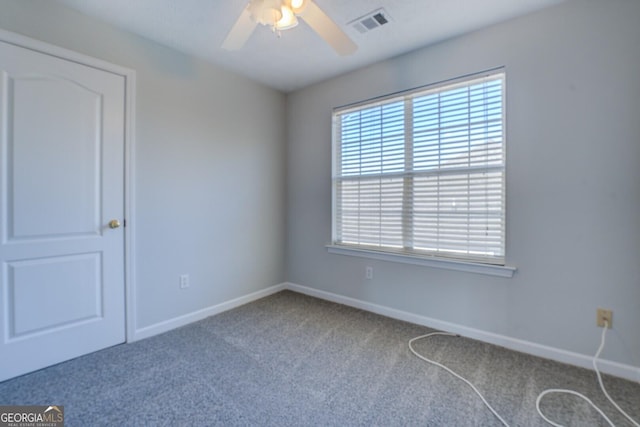 carpeted spare room with visible vents, baseboards, and ceiling fan