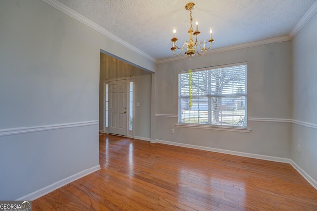 entrance foyer with ornamental molding, hardwood / wood-style flooring, a textured ceiling, an inviting chandelier, and baseboards