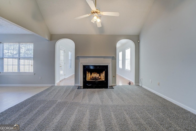 unfurnished living room featuring a fireplace with flush hearth, lofted ceiling, a ceiling fan, arched walkways, and baseboards