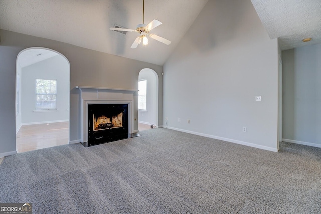 unfurnished living room featuring ceiling fan, high vaulted ceiling, carpet floors, a fireplace, and a textured ceiling