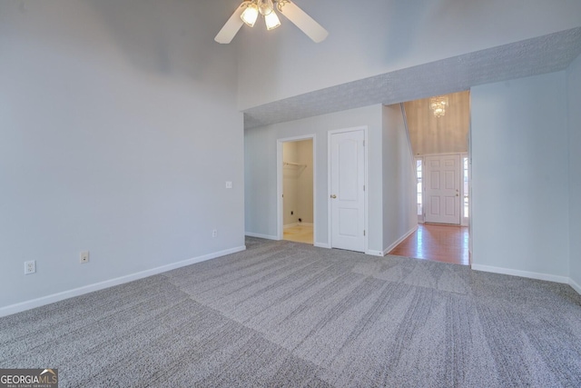 carpeted spare room with ceiling fan with notable chandelier, a high ceiling, and baseboards