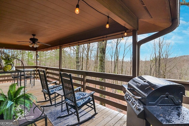 wooden deck with grilling area, a forest view, and ceiling fan