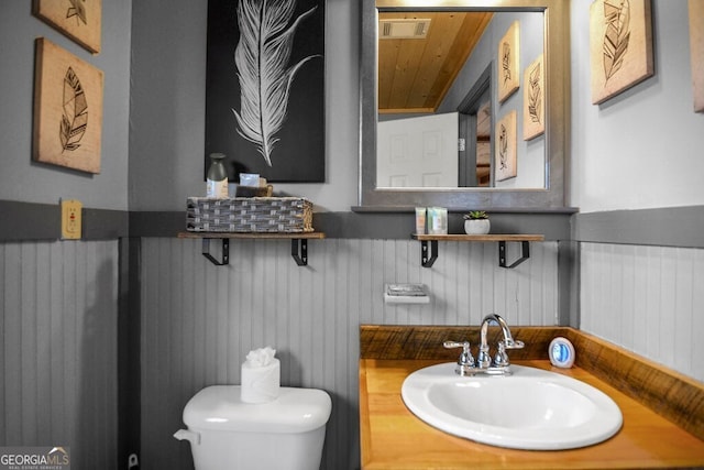 half bath with a sink, visible vents, toilet, and wainscoting