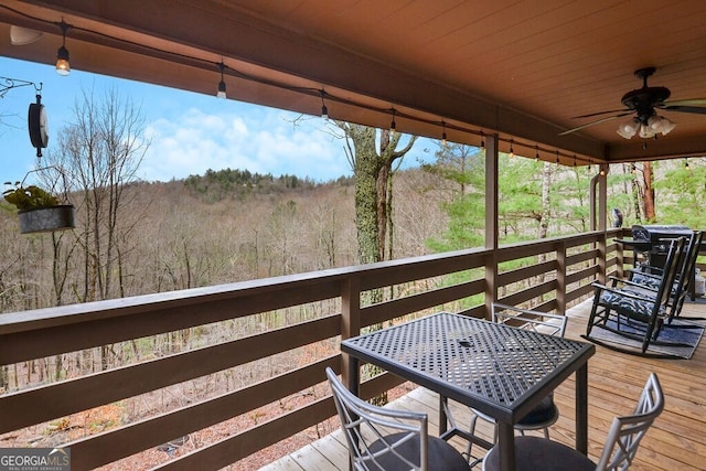 wooden deck featuring grilling area, a wooded view, and ceiling fan