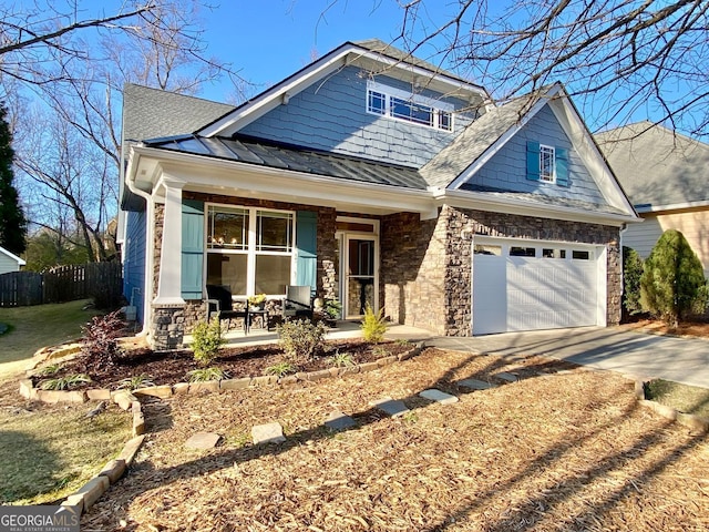 craftsman-style house with fence, driveway, a standing seam roof, a garage, and stone siding