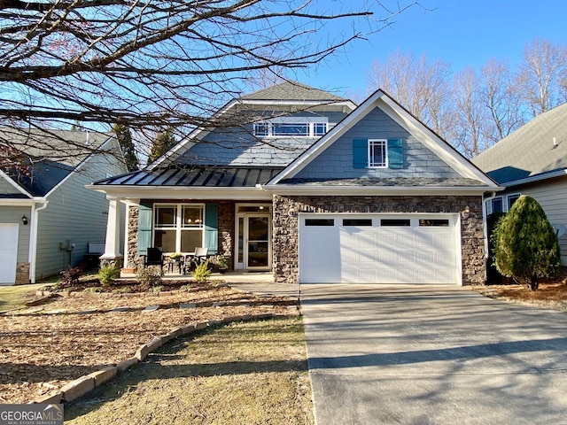 craftsman house featuring a standing seam roof, an attached garage, covered porch, concrete driveway, and stone siding