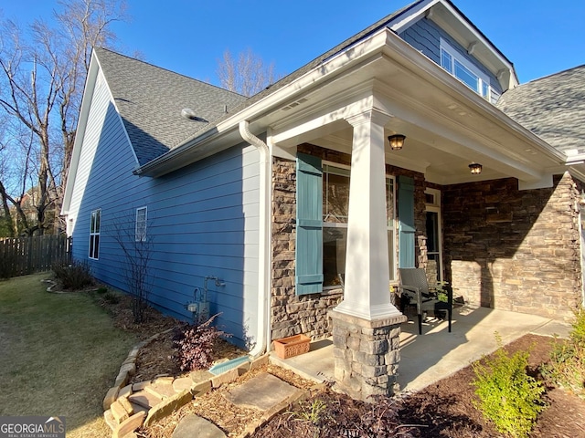 view of home's exterior with stone siding, covered porch, a lawn, and roof with shingles