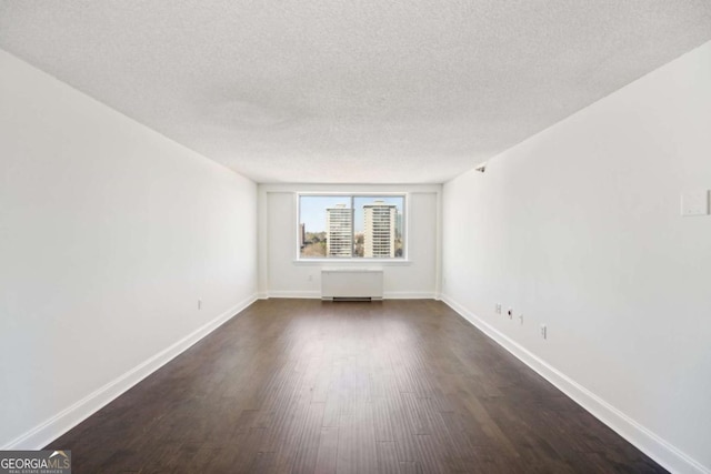 spare room featuring dark wood-style floors, a textured ceiling, and baseboards