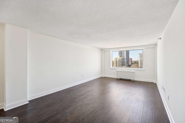 spare room with a textured ceiling, dark wood-style flooring, and radiator heating unit