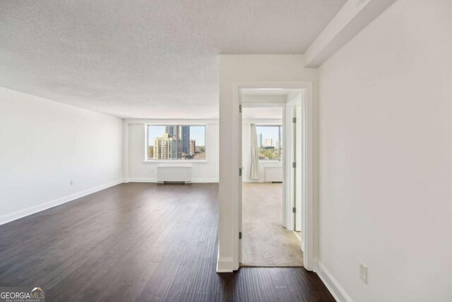 unfurnished living room featuring dark wood-style floors, a textured ceiling, and baseboards