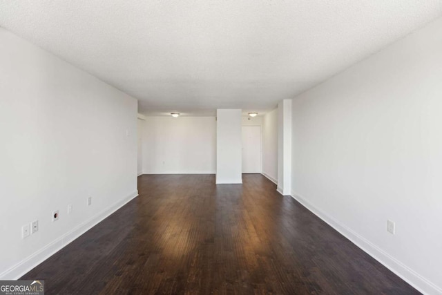 empty room with dark wood finished floors, a textured ceiling, and baseboards