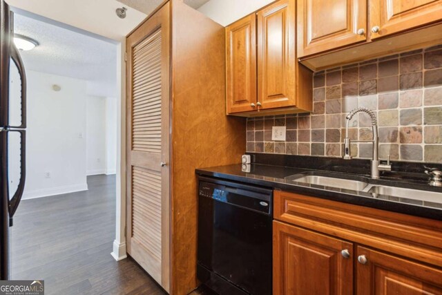 kitchen with a sink, tasteful backsplash, black appliances, and dark wood-style flooring