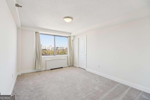 carpeted spare room featuring radiator, baseboards, a textured ceiling, and a city view