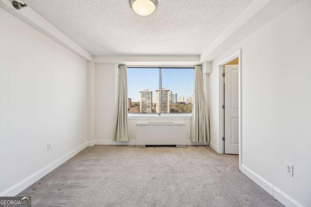 unfurnished room with a view of city, a textured ceiling, baseboards, and carpet