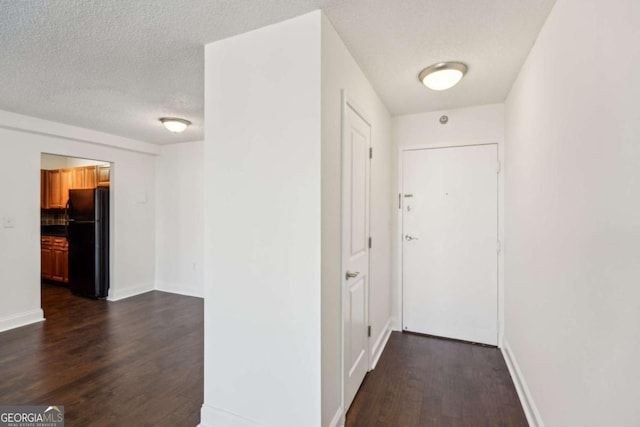 corridor with dark wood finished floors, baseboards, and a textured ceiling