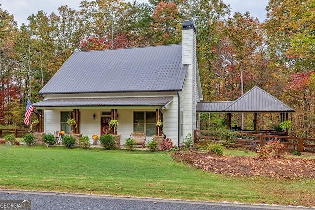 view of front of house featuring a porch, metal roof, a front yard, and a chimney