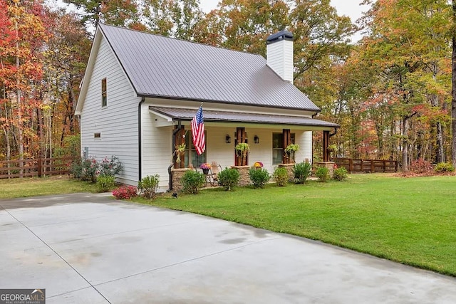 view of front facade with fence, covered porch, a front yard, metal roof, and a chimney