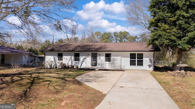 ranch-style house with concrete driveway, fence, and a front lawn