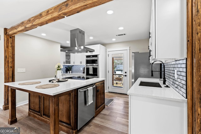 kitchen featuring visible vents, island exhaust hood, a sink, appliances with stainless steel finishes, and white cabinetry