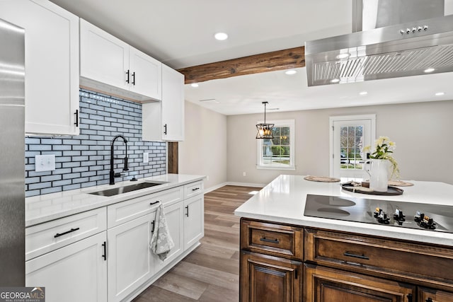 kitchen with beamed ceiling, a sink, wall chimney exhaust hood, black electric cooktop, and backsplash