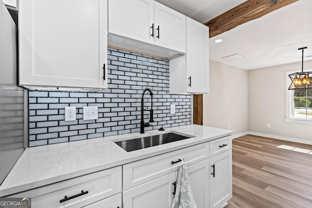 kitchen with baseboards, light wood-style flooring, a sink, white cabinets, and tasteful backsplash