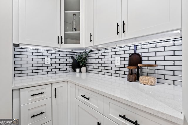 kitchen featuring white cabinetry, decorative backsplash, glass insert cabinets, and light stone countertops