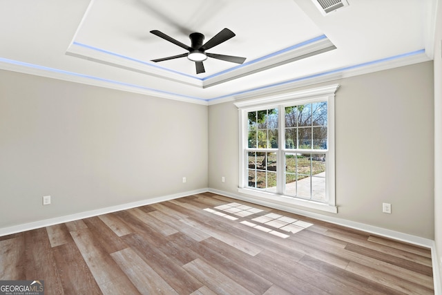 unfurnished room featuring a raised ceiling, wood finished floors, visible vents, and ceiling fan