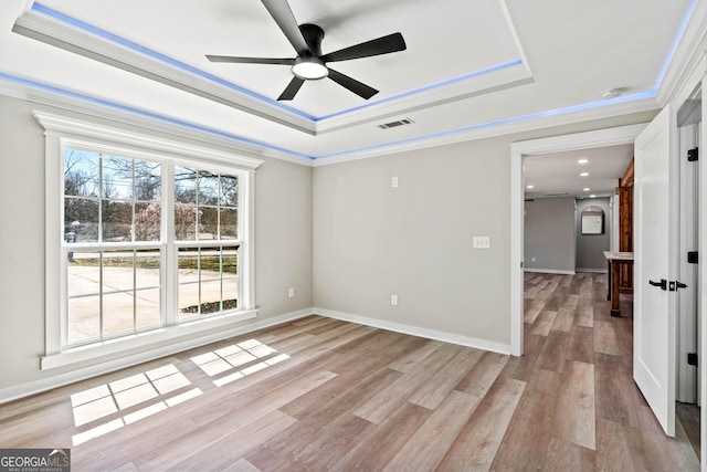 empty room with a tray ceiling, a ceiling fan, and light wood finished floors