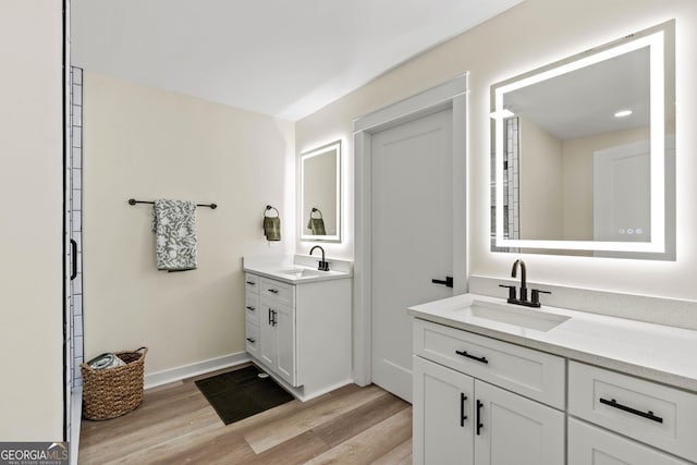 bathroom featuring wood finished floors, two vanities, baseboards, and a sink