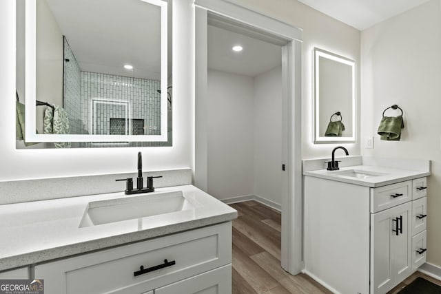 bathroom featuring a stall shower, wood finished floors, two vanities, and a sink