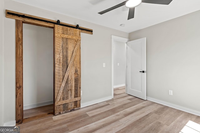 unfurnished bedroom featuring a ceiling fan, a barn door, baseboards, and light wood-type flooring