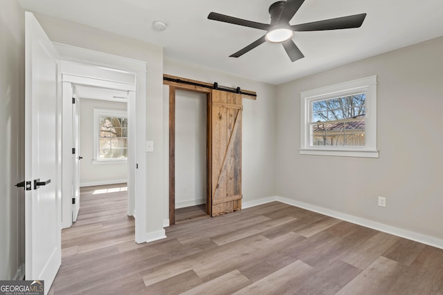 unfurnished bedroom with a ceiling fan, a barn door, light wood-style floors, and baseboards