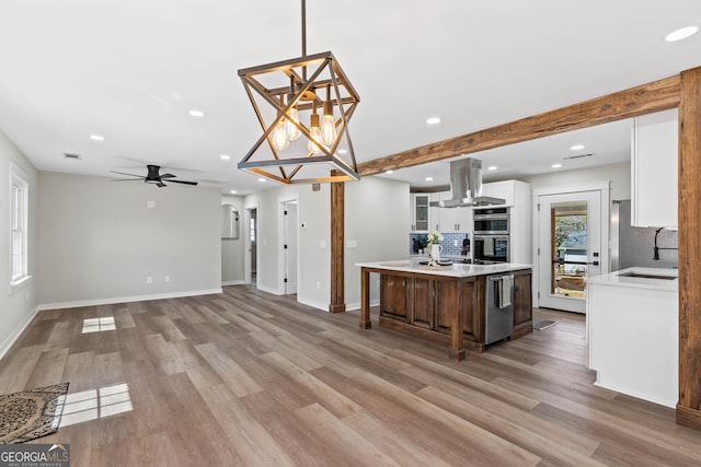 kitchen featuring island exhaust hood, light countertops, white cabinetry, light wood-type flooring, and a center island