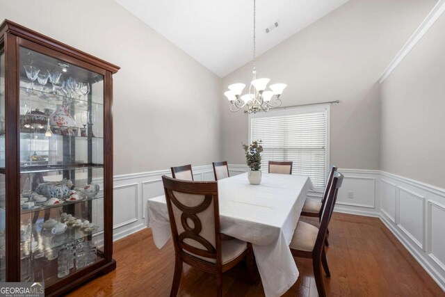 dining space featuring visible vents, a wainscoted wall, a notable chandelier, dark wood-type flooring, and vaulted ceiling