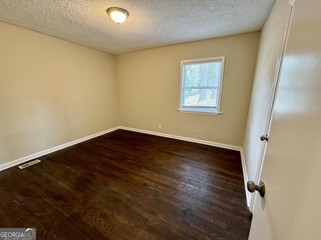 spare room with visible vents, baseboards, a textured ceiling, and dark wood finished floors