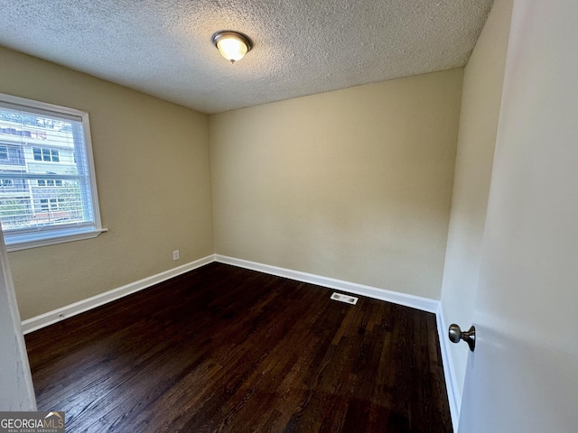 unfurnished room featuring visible vents, a textured ceiling, baseboards, and dark wood-style flooring