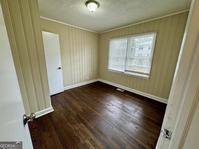 spare room featuring crown molding, a textured ceiling, dark wood-type flooring, and baseboards