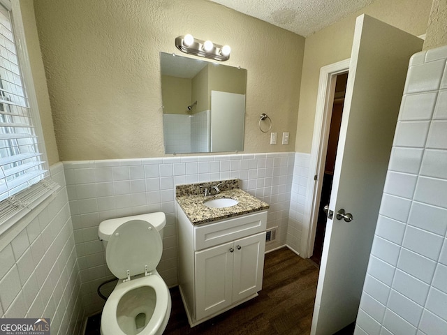 bathroom featuring a wainscoted wall, a textured ceiling, tile walls, and a textured wall