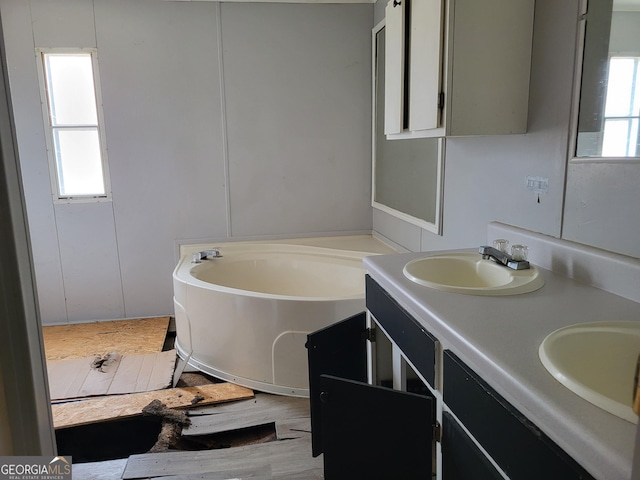 full bathroom with double vanity, wood finished floors, a garden tub, and a sink