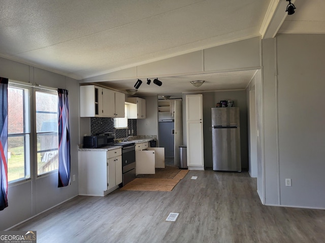 kitchen featuring light wood-type flooring, range with electric cooktop, white cabinetry, freestanding refrigerator, and vaulted ceiling