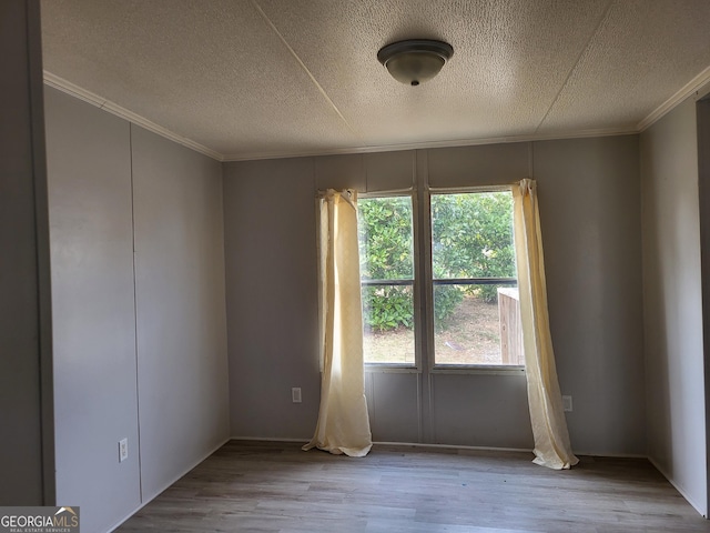 unfurnished room featuring a textured ceiling, wood finished floors, and ornamental molding