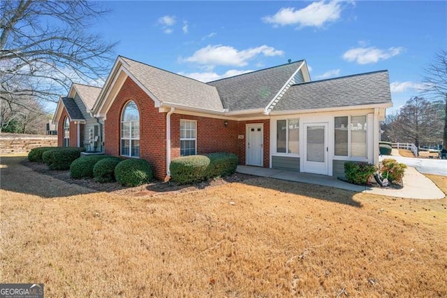 ranch-style house featuring brick siding, roof with shingles, and a front lawn