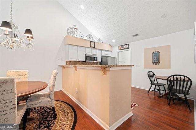 kitchen with a notable chandelier, dark wood-type flooring, a kitchen breakfast bar, appliances with stainless steel finishes, and a peninsula