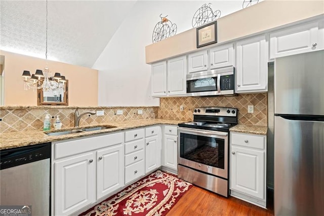 kitchen featuring vaulted ceiling, appliances with stainless steel finishes, wood finished floors, a notable chandelier, and a sink