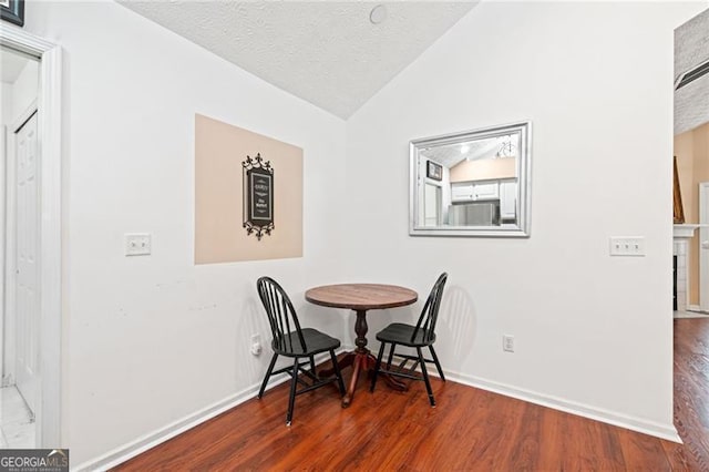 dining room featuring vaulted ceiling, wood finished floors, baseboards, and a textured ceiling