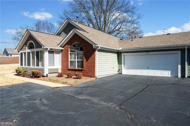 ranch-style house featuring aphalt driveway, roof with shingles, an attached garage, a sunroom, and brick siding