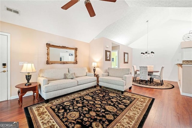 living area featuring visible vents, ceiling fan with notable chandelier, wood finished floors, and vaulted ceiling